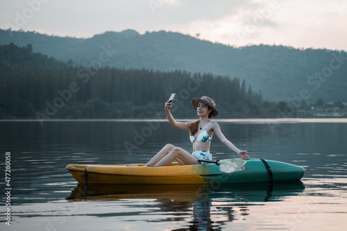 Kayaks in the lake. Tourists kayaking on mirror lake. taking photo when travel activity. woman playing in water in sunset. active woman rowing boat in lake with mountain view in evening. © Vajirawich