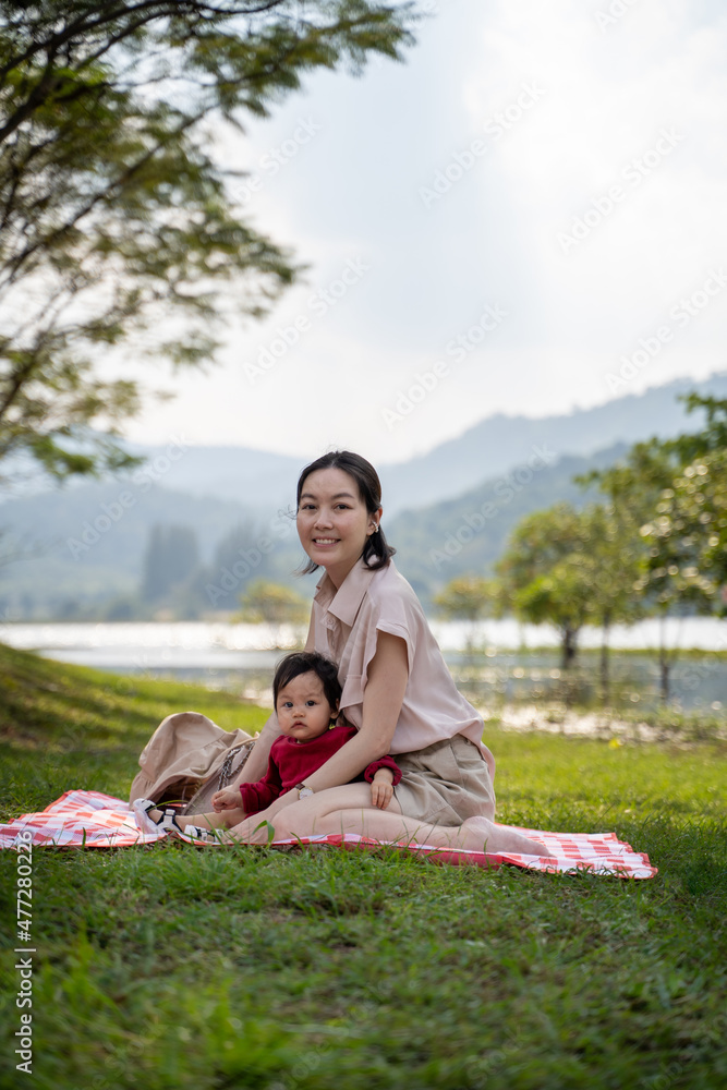Asian parent mother holding baby infant outdoors camping near lake. calm activity of family picnic in woodland pine trees mountain. baby toddler playing outdoor with mom. Asian parent mother holding baby infant outdoors camping near lake. calm activity of family picnic in woodland pine trees mountain. baby toddler playing outdoor with mom.