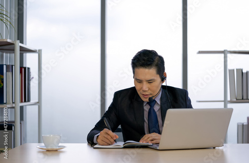 Asian Businessman in suit using headset with mic prepare for online meeting through laptop computer. Working concept Social Distancing, Quarantine, and Isolation