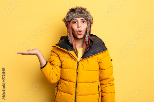 hispanic woman looking surprised and shocked, with jaw dropped holding an object. winter concept photo