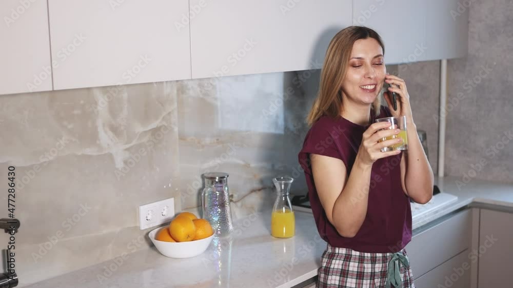 Portrait of young woman in the kitchen drinking juice and talking on the phone, 4K Portrait of young woman in the kitchen drinking juice and talking on the phone, 4K