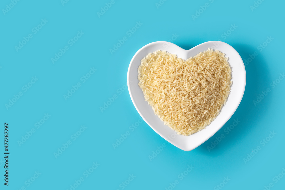 Raw rice on heart shaped plate on blue background.Copy space Raw rice on heart shaped plate on blue background.Copy space