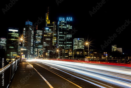 Traffic light rays on a street on a bridge in Frankfurt - Main at night with view to the skyline of the city at a cold day in winter. © ms_pics_and_more