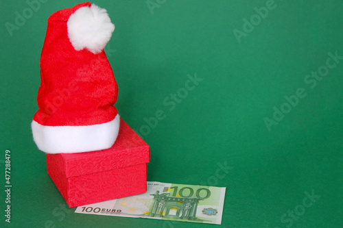 Christmas present. A red gift box with Santa Claus hat on it and a 10 Euro bill lying next to it