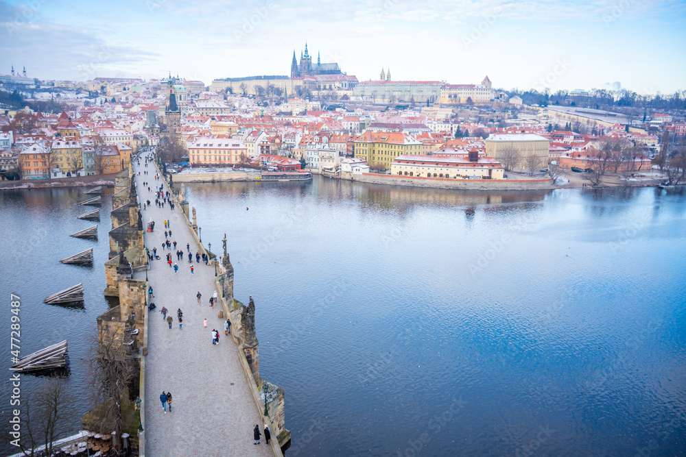 Fototapeta premium People are walking on Charles bridge, whose rooftops are covered by snow, Prague in the winter