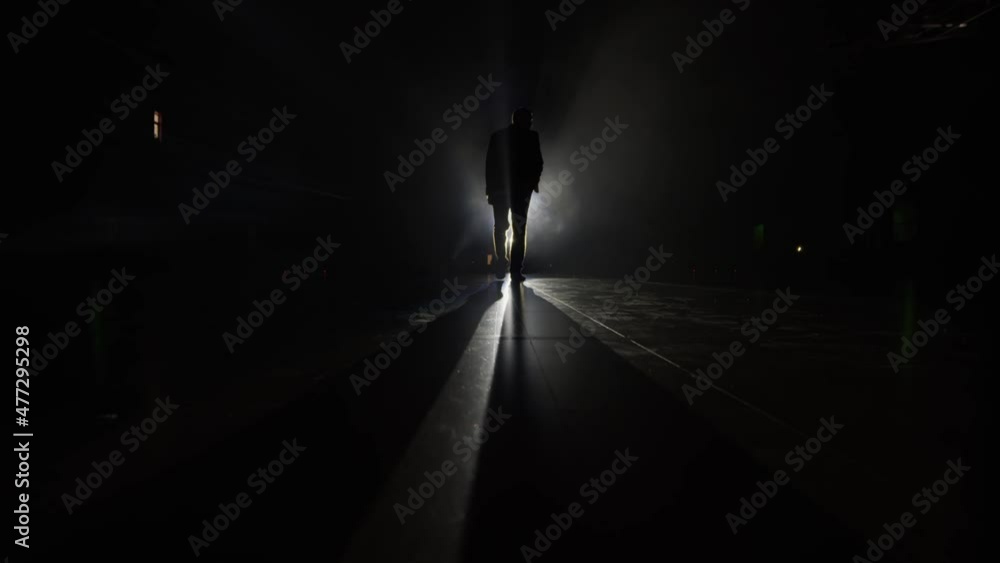 Silhouette of a man in a suit leaves the stage 4K. Mystical atmosphere, smoke, spotlight. Person in the dark