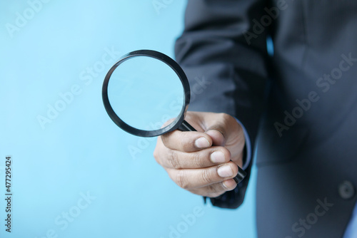 hand holding magnifying glass against blue background 