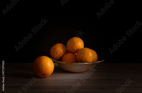 Kompozycja z pomarańczami w ceramicznym naczyniu. Owoce na ciemnym tle
