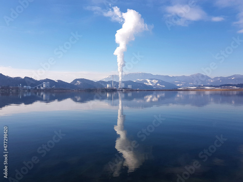 Winter view of Šoštanj Thermal power plant near Velenje from artificial lake created by coal mining, snow covered hills