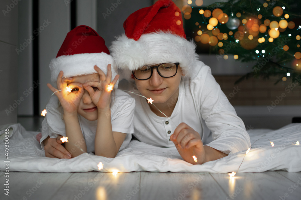 Fototapeta premium a boy in a Santa Claus hat and glasses lies on the floor and smiles