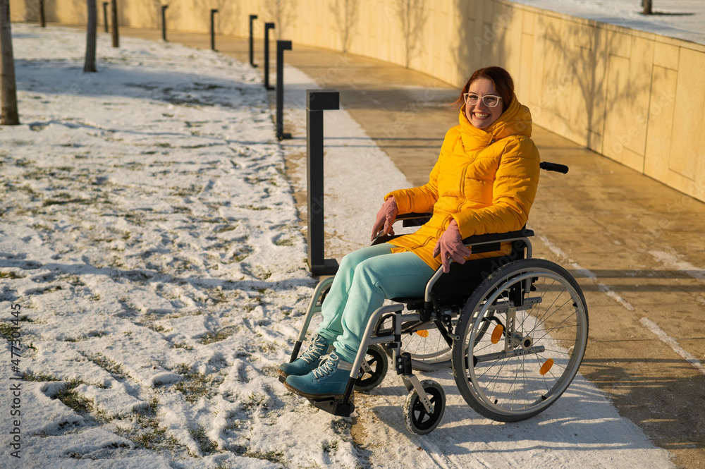 Obraz premium Caucasian woman with disabilities rides on a chair in the park in winter. Girl on a walk in a wheelchair. 