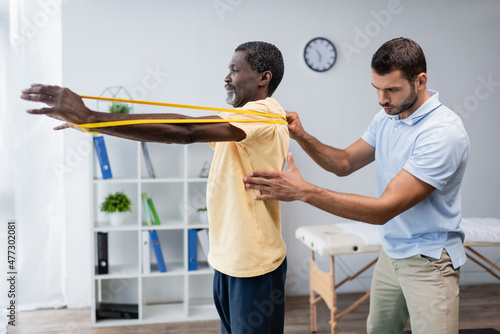 young physical therapist assisting mature african american man training with elastics
