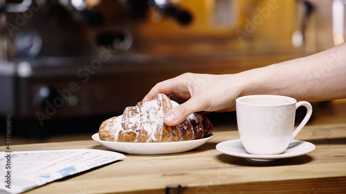 cropped view of man taking croissant in coffee shop.