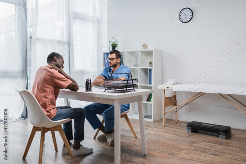 african american man suffering from neck pain on consultation with rehabilitologist