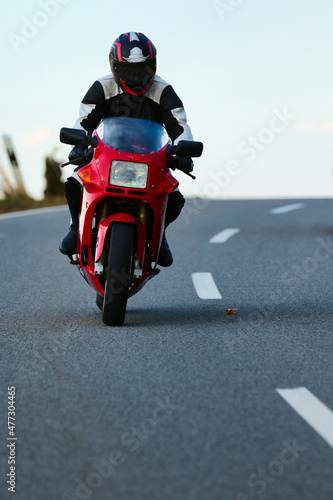 Red motorcycle with driver in leather suit while driving on a road with a slight side position  photographed from the front..