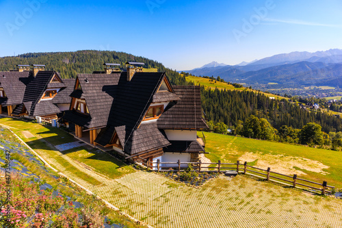 Beautiful wooden houses built in traditional style architecture on green meadow with view of Giewont and Tatra Mountains, Koscielisko, Poland photo