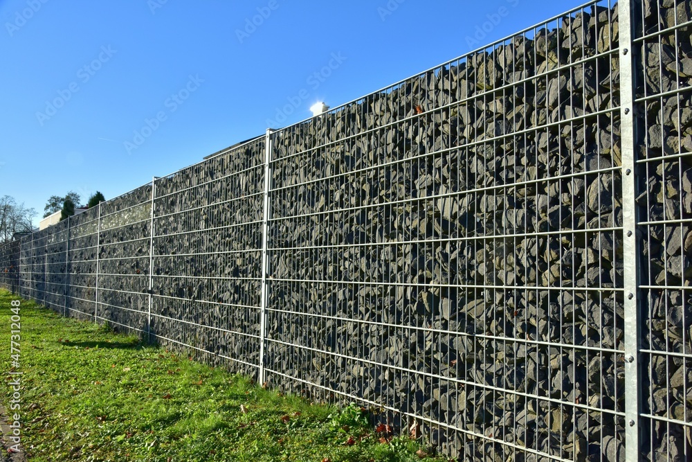 Fototapeta premium Moderner Sichtschutzzaun aus mit Naturstein gefüllten Gabionen um ein Neubaugebiet