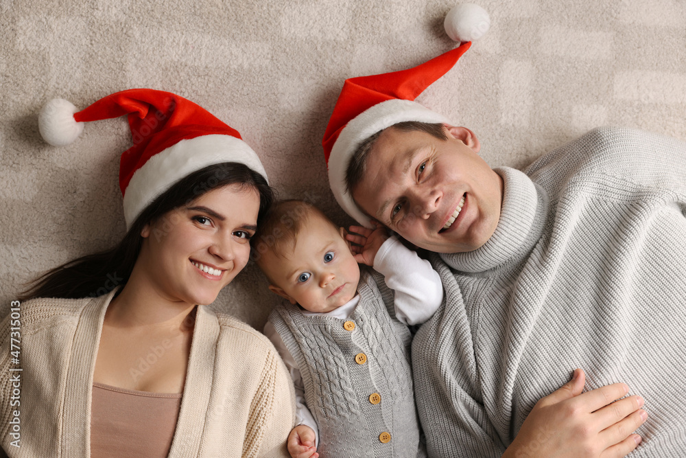 Fototapeta premium Happy couple with cute baby on floor, top view. Christmas celebration