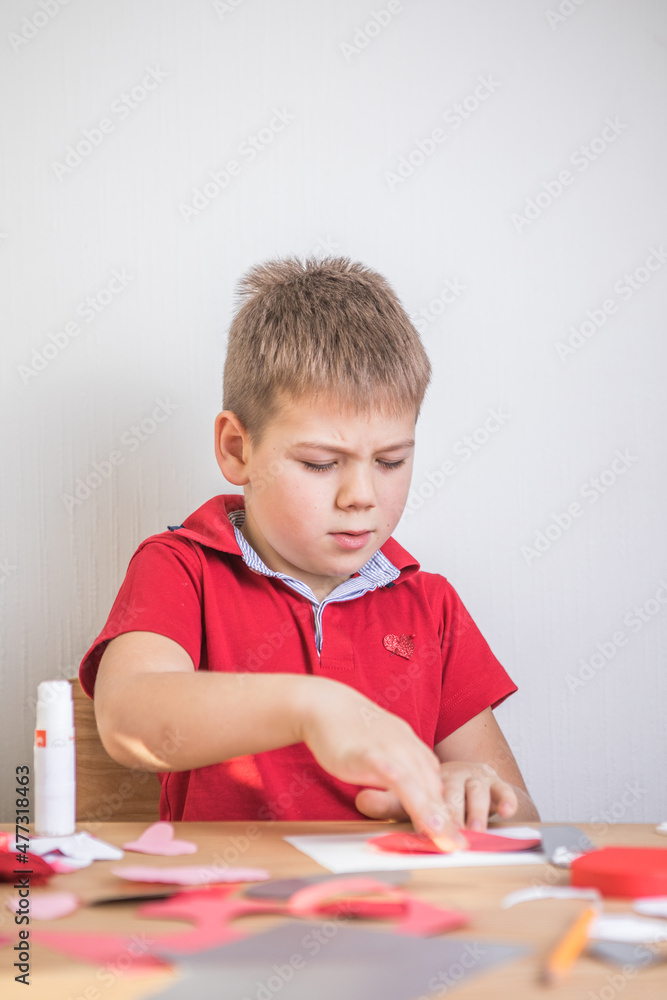 DIY holiday card with red paper heart, symbol of love. Kid boy makes Mother's Day, Valentine's Day, greeting card. Hobby, children art concept, gift with your own hands, DIY Ideas for children