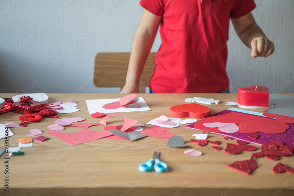 Fototapeta premium DIY holiday card with red paper heart, symbol of love. Kid boy makes Mother's Day, Valentine's Day, greeting card. Hobby, children art concept, gift with your own hands, DIY Ideas for children