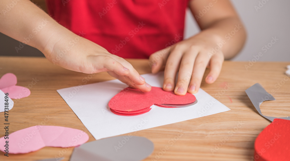 DIY holiday card with red paper heart, symbol of love. Kid boy makes Mother's Day, Valentine's Day, greeting card. Hobby, children art concept, gift with your own hands, DIY Ideas for children DIY holiday card with red paper heart, symbol of love. Kid boy makes Mother's Day, Valentine's Day, greeting card. Hobby, children art concept, gift with your own hands, DIY Ideas for children