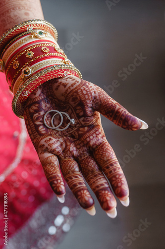 Canvas Print Woman hands with henna holding two white gold wedding rings on grey background I