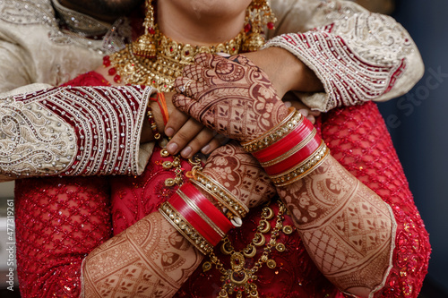 Canvas Print Indian bride in red wedding costume holds groom's hands on her chest while he hu