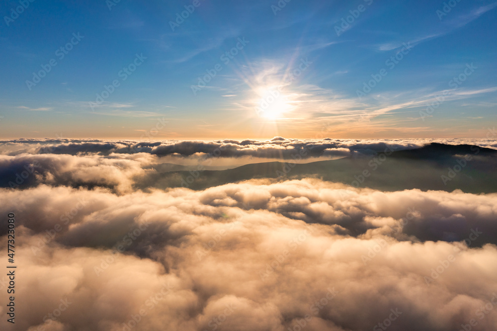 Sun shining above layer of white fluffy clouds at sunset Sun shining above layer of white fluffy clouds at sunset