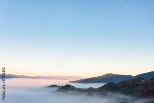 Highland with colorful forests covered with fog at sunrise