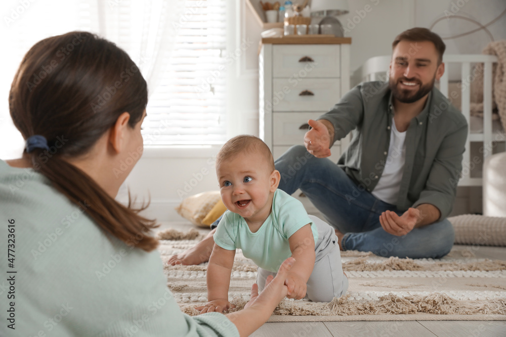 Happy parents helping their baby to crawl on floor at home Happy parents helping their baby to crawl on floor at home