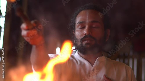 Close-up of young indian man leads Fire ceremony Agni hotra, Hindu rituals, Yagya. He pours Ghee oil into the fire, sings mantras. Slow motion.
