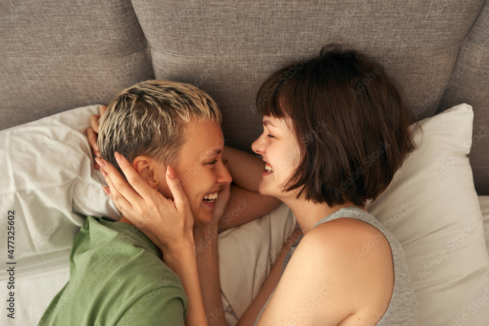 Young laughing lesbian couple rest and hug on bed Young laughing lesbian couple rest and hug on bed