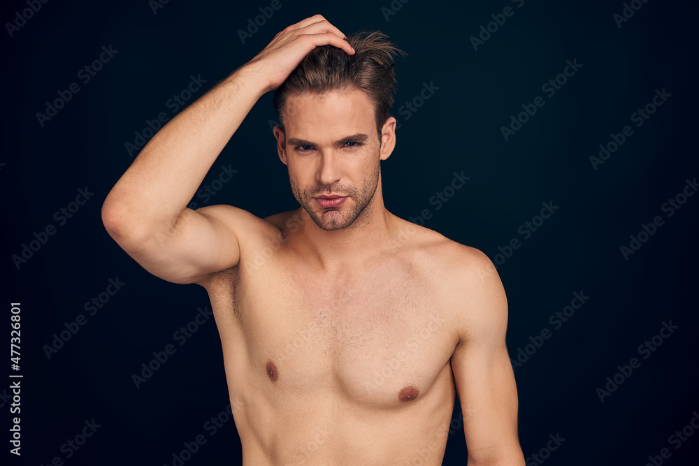 Everything must be perfect. Charming young man keeping hands in hair and smiling while standing against dark blue background.
