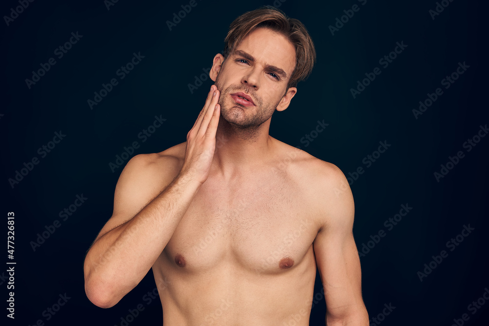 Handsome man. Charming young man keeping hand on chin while standing against dark blue background.