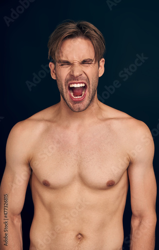 Portrait of a athleltic muscular man screaming isolated on a dark blue background
