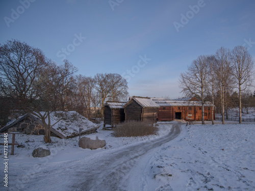 Old log stable and houses with birch-bark roofs in a snowy park a sunny winter day afternoon in Stockholm