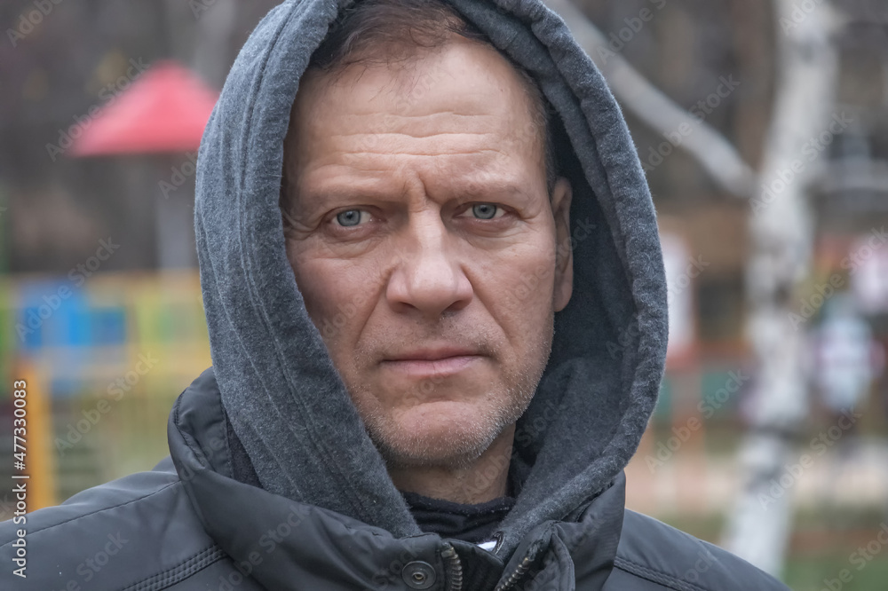 brutal handsome man, middle-aged, 55-60 years old, stands in the park in a gray sweatshirt with a hood on his head brutal handsome man, middle-aged, 55-60 years old, stands in the park in a gray sweatshirt with a hood on his head