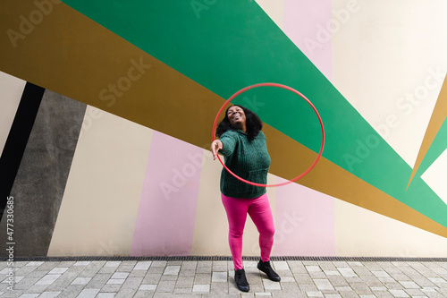 Cheerful plus size woman playing with plastic hoop on footpath photo