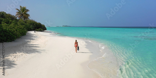 Young woman in a red bikini holding snorkeling gear while walking down a white sand beach. Dhigurah island, Maldives. photo