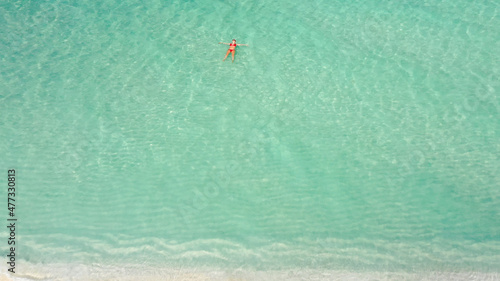 Young woman in a red bikini floating in turquoise sea nearby beach. Dhigurah island, Maldives. photo