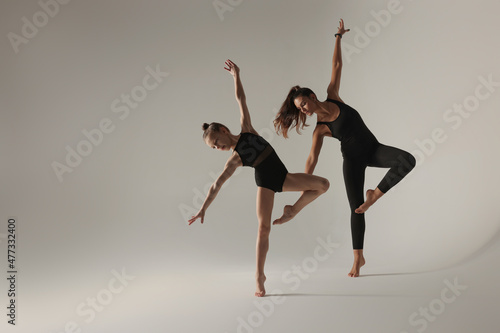 Little girl and her coach doing gymnastic exercise on white background