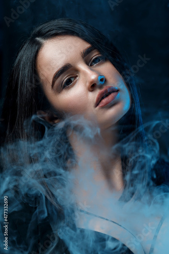 Fototapeta Naklejka Na Ścianę i Meble -  young brunette woman with professional makeup in a black jacket in the studio. multicolored light with smoke