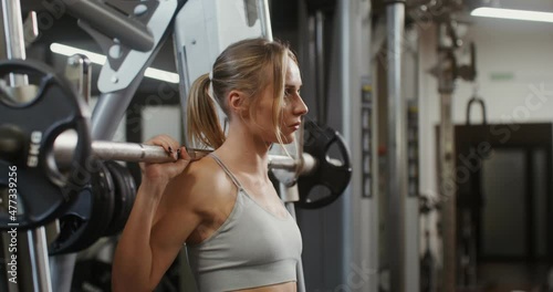 Young woman quats with a barbell with weights using an exercise machine photo