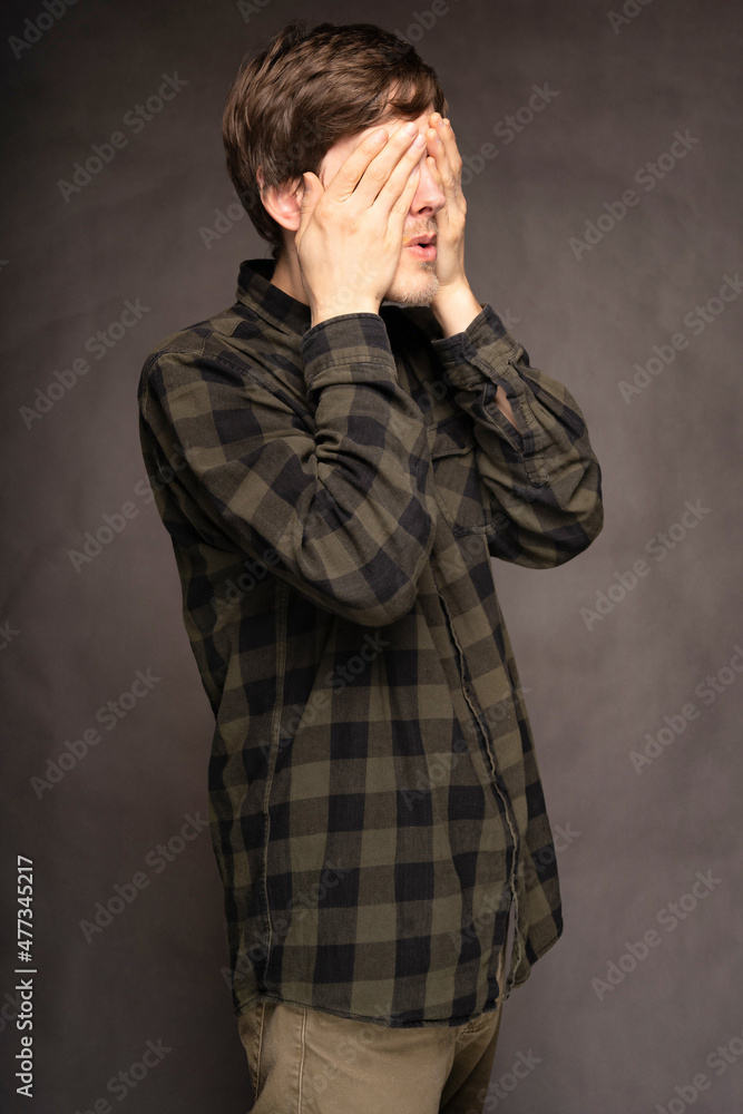 Young handsome tall slim white man with brown hair covering both eyes with flannel shirt on grey background Young handsome tall slim white man with brown hair covering both eyes with flannel shirt on grey background