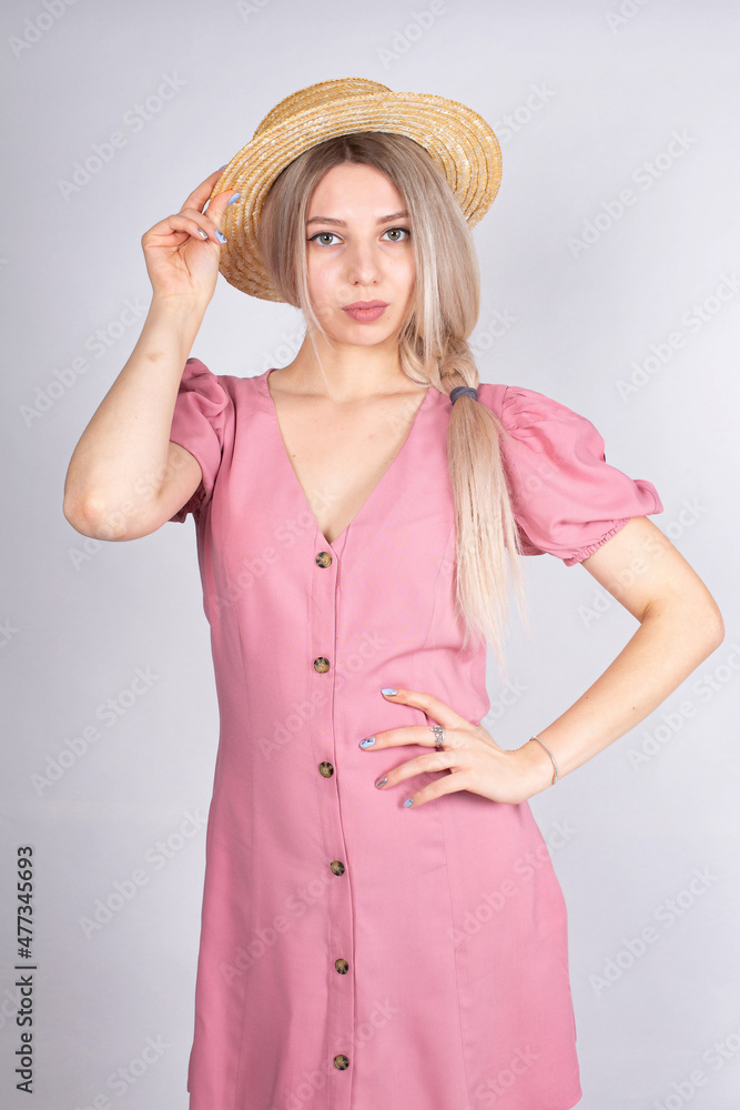 Woman with blonde hair and white skin isolated on grey in hat and rose dress Woman with blonde hair and white skin isolated on grey in hat and rose dress