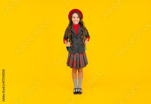 smiling child in school uniform and beret full length on yellow background, schoolgirl