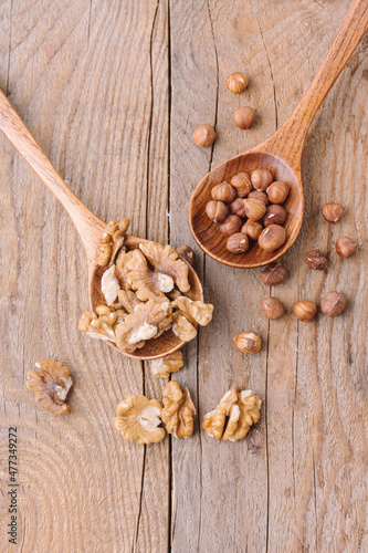 Peeled walnuts and hazelnuts in spoon on wooden background. Two spoons. Different nuts