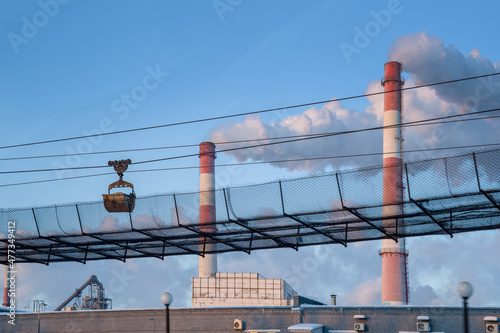 Factory chimneys from which smoke comes out. In the foreground is the cable car. Carts transport raw materials.