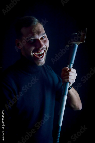 portrait of a scary young man laughing evil with an ax in his hand