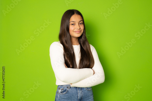 Portrait of a smiling young girl with long brunette hair in winter clothing standing with arms folded isolated over green background